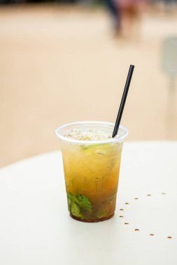 Beyaz masa üzerinde limon ve nane ile plastik bir bardak Mojito kokteyli..
