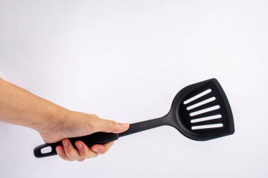 Hand and plastic black spatula for a frying pan isolated on white background.