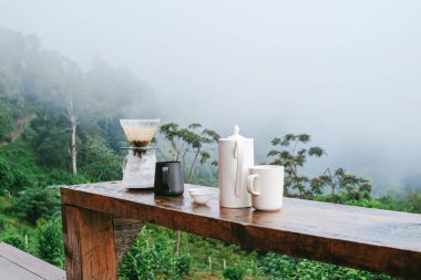 Arka planda dağ manzaralı ahşap masaya damlatılmış kahve seti