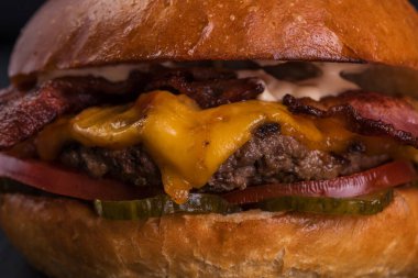 Köfteli hamburger, pastırma, peynir, turşu, domates ve sos siyah ahşap arka planda..