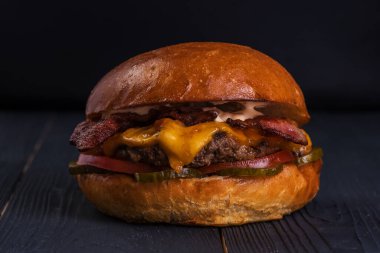 Köfteli hamburger, pastırma, peynir, turşu, domates ve sos siyah ahşap arka planda..