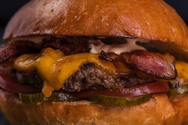 Köfteli hamburger, pastırma, peynir, turşu, domates ve sos siyah ahşap arka planda..