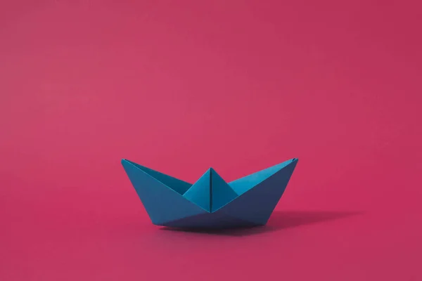Pembe arka planda mavi origami kağıt tekne. Asgari konsept.