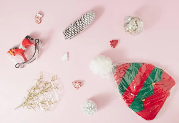 Soluk pembe arka planda plastik folyoya sarılı Noel süsleri. Asgari konsept.