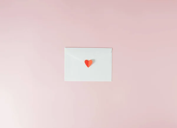 Valentine's Day love letter in a white envelope on a pale pink background sealed with a red heart. Minimal concept.