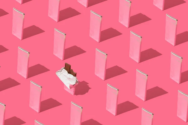 Alüminyum folyoya sarılı çikolata kalıpları ve pembe arka planda paketlenmemiş bir çubuk..