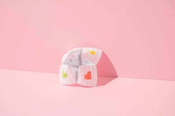 Kağıt origami falcısı pembe arka plana yaslanıyor. Asgari konsept.
