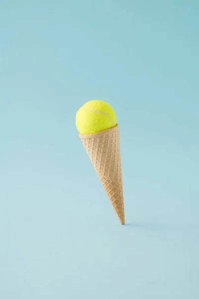 Arka planda süzülen sarı tenis toplu dondurma külahı. Asgari konsept.