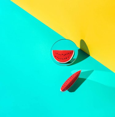 Mavi ve sarı arka planda aynanın önünde duran plastik karpuz. Asgari yaz konsepti.