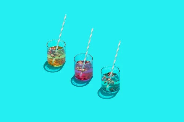 Three colourful drink cocktail glasses with paper straws on blue background.