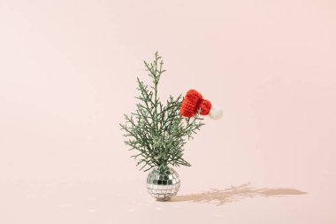 Mutlu Noeller asgari konsept. Yeşil dallı disko topu ve soluk pembe arka planda kırmızı Noel Baba şapkası..