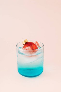 Kırmızı Noel mücevheri, eriyen buzun içinde mavi bardakta yüzüyor. Yeni yıl selamları. Asgari konsept.