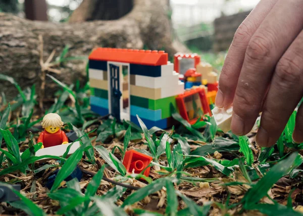 Hand building up lego brick house on grass — Stock Photo, Image