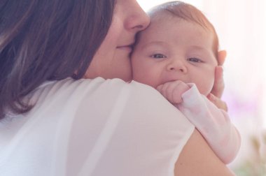 Anne ve yeni doğmuş bebeği. Anne küçük kızını kucağında tutuyor. Güneş ışığı efektli fotoğraf, yumuşak doğal ışık, seçici odaklı..