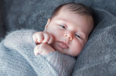 Yeni doğmuş bebek sıcak bir battaniyeye sarılmış. Uyanmış ve etrafına bakınan yeni doğmuş bir bebeğin güzel yakın plan portresi. Çocuk battaniyenin kolunu çekti..