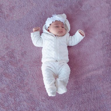 Mor arka planda yeni doğmuş bir bebek, tepeden çekilmiş bir resim. Yeni doğmuş. Çocuk sıkı giyinmiş.. 