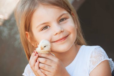 Mutlu küçük kız elinde bir tavuk tutuyor. Kümes hayvanlı çocuk. Kızların elindeki civcivin yakın görüntüsü. Seçici odak ve sıcak renkli bir fotoğraf. Evcil hayvanlar. 