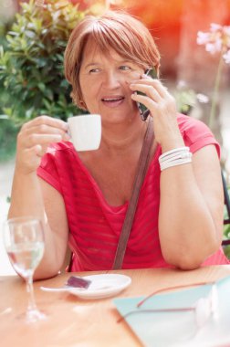 Akıllı telefondan konuşan ve kafede kahve içen olgun bir kadın. Emekli kadın sohbet ediyor. Yetişkinler için eğitim.