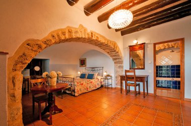 Kır evinde ya da otelde kırsal tarzda güzel, sıcak bir yatak odası. Tahta kirişler ve doğal taştan yapılmış duvarlar. Akdeniz tarzı ev.