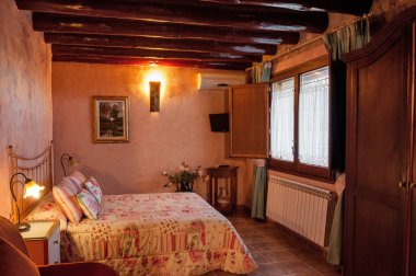 Kır evinde ya da otelde kırsal tarzda güzel, sıcak bir yatak odası. Tahta kirişler ve doğal taştan yapılmış duvarlar. Akdeniz tarzı ev.