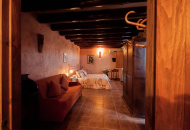 Kır evinde ya da otelde kırsal tarzda güzel, sıcak bir yatak odası. Tahta kirişler ve doğal taştan yapılmış duvarlar. Akdeniz tarzı ev.