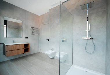 Cam küveti ve lüks lavabosu olan modern bir banyo. Duvarlar ve zemin modern fayanslarla kaplı.. 