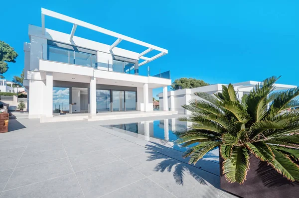 奢华的现代白色房子 窗户很大 俯瞰着一个有着棕榈树和蓝色游泳池的美丽花园 高科技风格的房子 — 图库照片