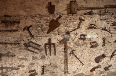 Antika duvarda asılı eski vintace aletleri. Yaba, kürek, demir, testere, eski kilit ve anahtarlar, çekiç, tırpan, bıçaklar, kazma, tırpan. Paslı demir metal aletler. 