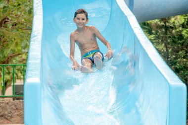 Su parkındaki mutlu çocuk kayıyor. Su parkında su kaydırağı. Mutlu çocukluk. 