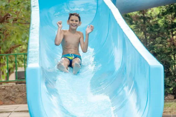 Happy boy in the water park going down the slide. Water slide in a water park. Happy childhood.