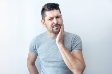 Diş ağrısı konsepti. Hüsrana uğramış genç adam yanağına dokunuyor ve korkunç bir diş ağrısı çekiyor.. 