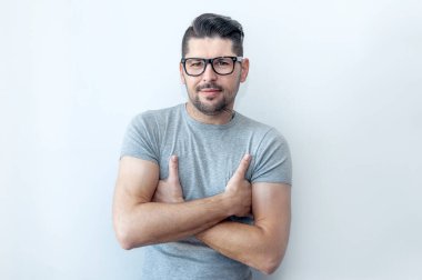 Gözlüklü, gri tişörtlü, duvarlara yaslanmış ve elleri çapraz olan zeki bir genç. .