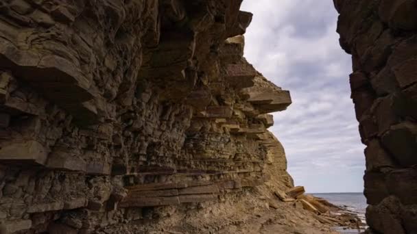 Camera beweging van een rotsachtige kust met getijdenpoelen naar de zee. Met een cape op de achtergrond — Stockvideo