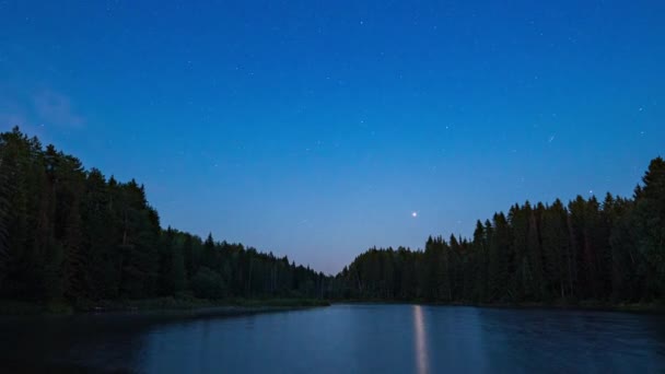 Cielo nocturno con nubes iluminadas por estrellas sobre un lago de montaña y una silueta de árboles. — Vídeos de Stock