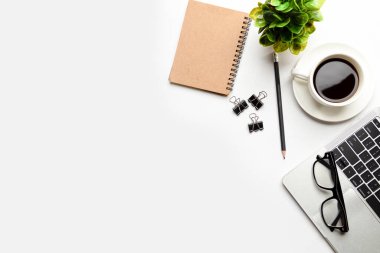 Üst kattaki ofis masasında yatıyordu. Çalışma alanı boş dizüstü bilgisayar, ofis malzemeleri, kalem, yeşil yaprak ve beyaz arka planda kahve fincanı.