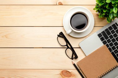 Üst kat ofis masası. Çalışma alanı boş, ofis malzemeleri, dizüstü bilgisayar, kalem, yeşil yaprak ve ahşap zemin üzerinde kahve fincanı.