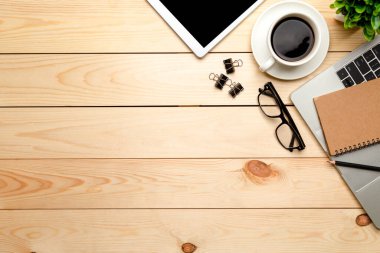 Üst kat ofis masası. Çalışma alanı boş, ofis malzemeleri, dizüstü bilgisayar, kalem, yeşil yaprak ve ahşap zemin üzerinde kahve fincanı.