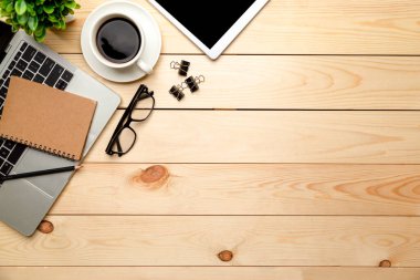 Üst kat ofis masası. Çalışma alanı boş, ofis malzemeleri, dizüstü bilgisayar, kalem, yeşil yaprak ve ahşap zemin üzerinde kahve fincanı.