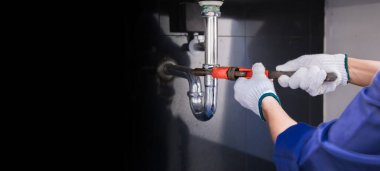 Tesisatçı ayarlanabilir anahtarla beyaz lavabo borusunu tamir ediyor..