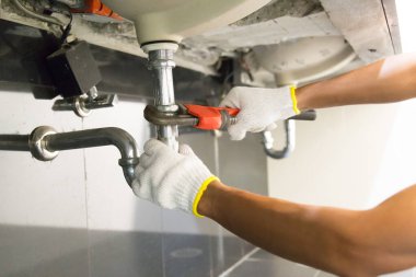 Tesisatçı ayarlanabilir anahtarla beyaz lavabo borusunu tamir ediyor..