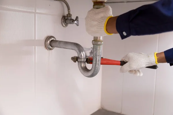 Tesisatçı ayarlanabilir anahtarla beyaz lavabo borusunu tamir ediyor..