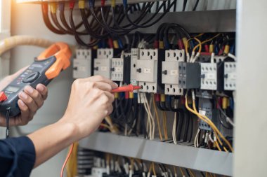 Elektrik mühendisi elektrik kabinesi kontrolündeki voltaj ve elektrik akımını ölçen bir testçi, elektrik sisteminin işleyişini konsept olarak kontrol ediyor .