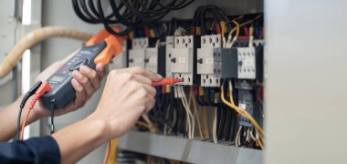Elektrik mühendisi elektrik kabinesi kontrolündeki voltaj ve elektrik akımını ölçen bir testçi, elektrik sisteminin işleyişini konsept olarak kontrol ediyor .