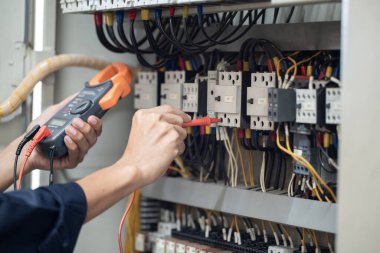Elektrik mühendisi elektrik kabinesi kontrolündeki voltaj ve elektrik akımını ölçen bir testçi, elektrik sisteminin işleyişini konsept olarak kontrol ediyor .
