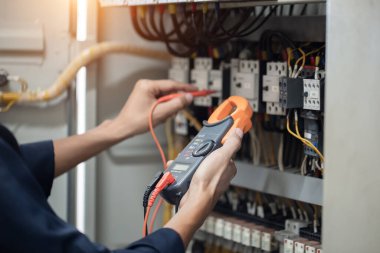 Elektrik mühendisi elektrik kabinesi kontrolündeki voltaj ve elektrik akımını ölçen bir testçi, elektrik sisteminin işleyişini konsept olarak kontrol ediyor .