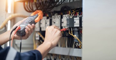 Elektrik mühendisi elektrik kabinesi kontrolündeki voltaj ve elektrik akımını ölçen bir testçi, elektrik sisteminin işleyişini konsept olarak kontrol ediyor .