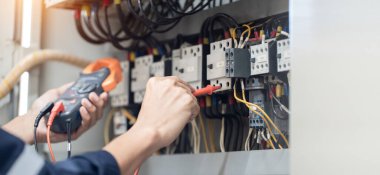 Elektrik mühendisi elektrik kabinesi kontrolündeki voltaj ve elektrik akımını ölçen bir testçi, elektrik sisteminin işleyişini konsept olarak kontrol ediyor .