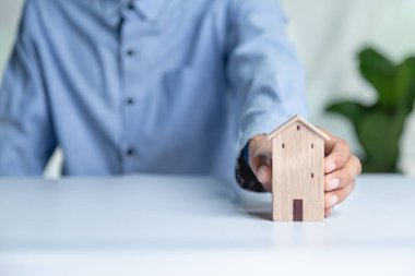 İş adamı ahşap masadan küçük ahşap ev modelini seçiyor, mülk almayı planlıyor. En iyisini seç konsepti.