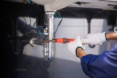 Tesisatçı ayarlanabilir anahtarla beyaz lavabo borusunu tamir ediyor..