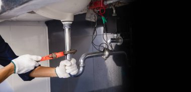 Tesisatçı ayarlanabilir anahtarla beyaz lavabo borusunu tamir ediyor..